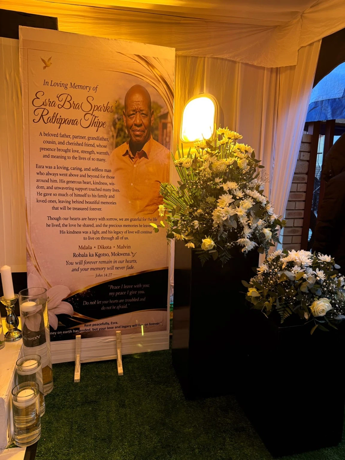 A Tribute in Full — A full view of the remembrance stage, with coordinated floral pedestals, welcome panels and a softly illuminated ceiling.